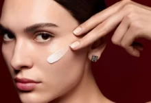 Модель с мазком тонального средства на скуле и серьгой Givenchy на бордовом фоне
