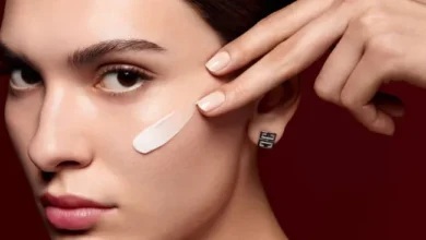 Модель с мазком тонального средства на скуле и серьгой Givenchy на бордовом фоне