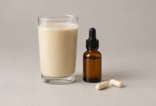Protein shake in a glass next to a dropper bottle and two capsules