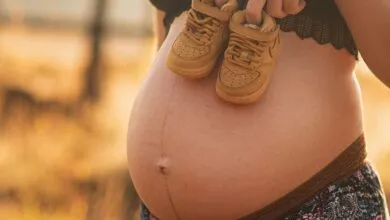 Pregnant woman outdoors holding baby shoes on her belly, symbolizing motherhood.