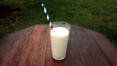 A refreshing glass of milk with a straw on a wooden table set outdoors, perfect for a healthy break.