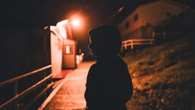 A captivating silhouette of a person walking through a dimly illuminated village at night.