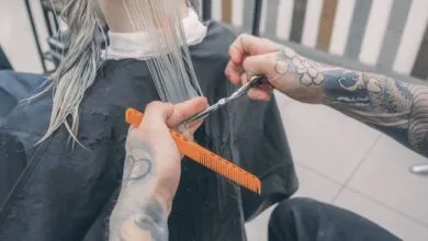 Close-up of a stylist's tattooed hands cutting wet hair in a modern beauty salon.