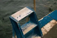 Rustic blue wooden ladder on a dock beside a serene lake, creating a vintage, nautical scene.