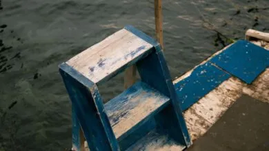 Rustic blue wooden ladder on a dock beside a serene lake, creating a vintage, nautical scene.