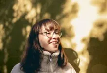 Portrait of a young woman with glasses enjoying sunlight outdoors, capturing a joyful moment.