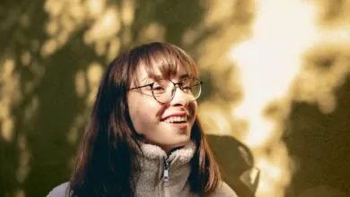 Portrait of a young woman with glasses enjoying sunlight outdoors, capturing a joyful moment.