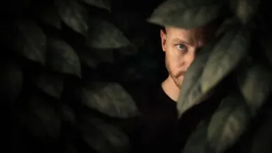 A man with one eye visible peers through thick leaves, creating a mysterious and intriguing effect.