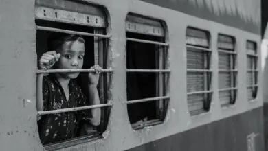 Black and white photo of a child looking pensively out of a train window, conveying emotion.