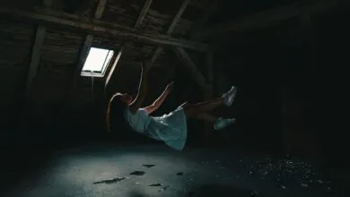 A surreal photograph of a woman in a white dress floating in an abandoned attic, capturing a sense of mystery.