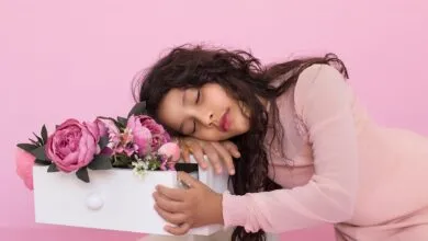 Young woman in pink dress resting with floral arrangement on pink background.