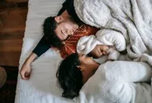 Top view of happy young multiethnic family with adorable newborn baby lying and sleeping on comfortable bed in sunny morning