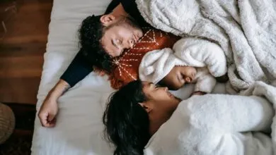 Top view of happy young multiethnic family with adorable newborn baby lying and sleeping on comfortable bed in sunny morning