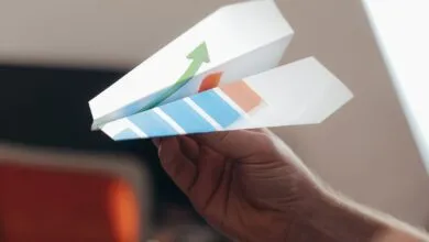 A close-up view of a hand holding a paper airplane with colorful graphics.