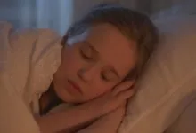 A young girl sleeping peacefully indoors, bathed in warm light.