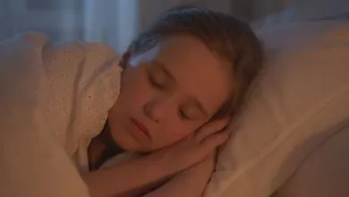 A young girl sleeping peacefully indoors, bathed in warm light.