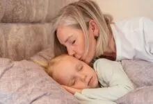 A loving grandmother kisses her sleeping grandchild in a cozy bedroom setting.