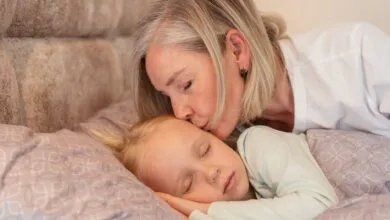 A loving grandmother kisses her sleeping grandchild in a cozy bedroom setting.