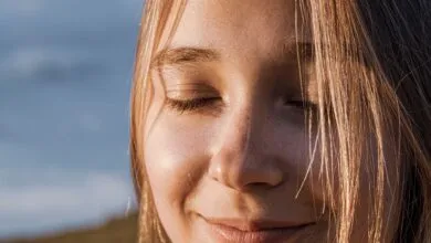 Close-up of a smiling woman with closed eyes, sunlit hair, and a serene expression outdoors.