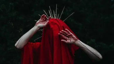 Moody fantasy portrait featuring hands in red fabric with thorny crown outdoors.