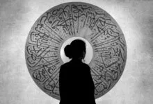 Silhouette of a woman standing before an ornate Arabic calligraphy artwork creating a striking monochrome effect.