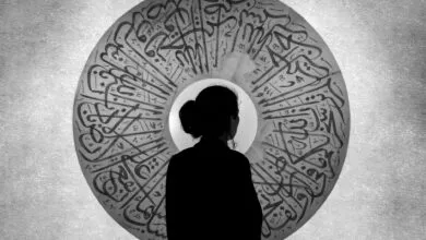 Silhouette of a woman standing before an ornate Arabic calligraphy artwork creating a striking monochrome effect.