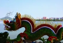Colorful dragon sculpture by a serene lake in Taiwan, with city skyline in the background.