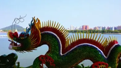Colorful dragon sculpture by a serene lake in Taiwan, with city skyline in the background.