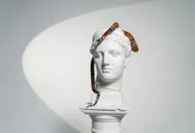 A white gypsum head sculpture with a snake elegantly draped over it, blending art and nature.