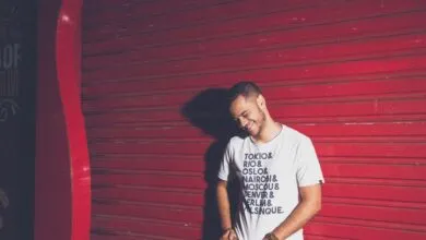 Casually dressed young man posing playfully against a vibrant red steel shutter with text t-shirt design.
