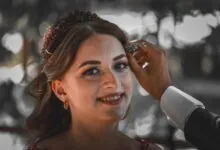 Close-up of a smiling bride being adorned with jewelry, showcasing an intimate wedding moment.