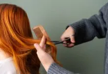 Close-up of red hair being trimmed with scissors and comb on green background.