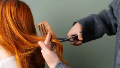 Close-up of red hair being trimmed with scissors and comb on green background.