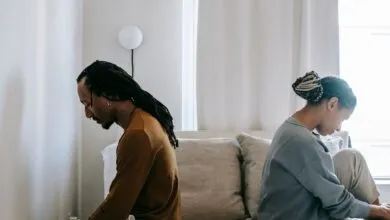 Side view unhappy sorrowful African American couple sitting on bed back to back after having argument
