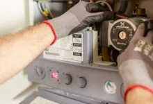 Мастер в рабочих перчатках обслуживает открытую газовую колонку: насос, манометр и панель управления