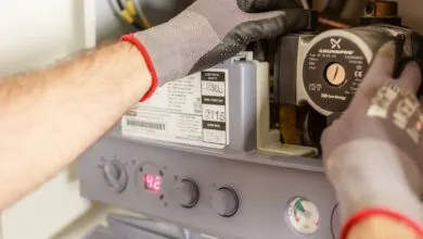 Мастер в рабочих перчатках обслуживает открытую газовую колонку: насос, манометр и панель управления